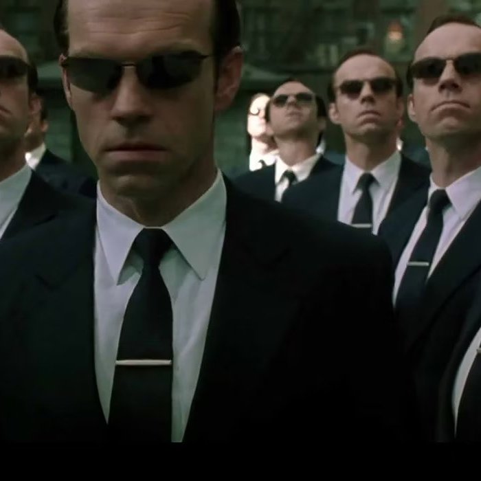 Still from The Matrix movies, showing multiple identical copies of a menacing looking man dressed in a sharp suite and dark glasses (Mr. Smith)