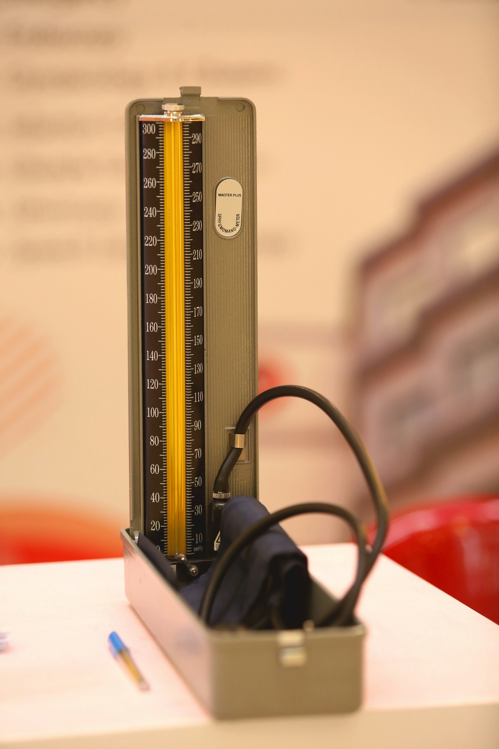 a photo of an anaolog blood pressure meter, including a cuff with tube neatly coiled, and a vertical bar with markers for different pressure levels in two scales