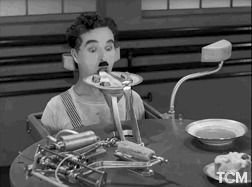 Animation from Charlie Chaplin's 'Modern Times'. Chaplin is seated, strapped in to a table, while a machine shoves bites of food into his mouth from a plate.