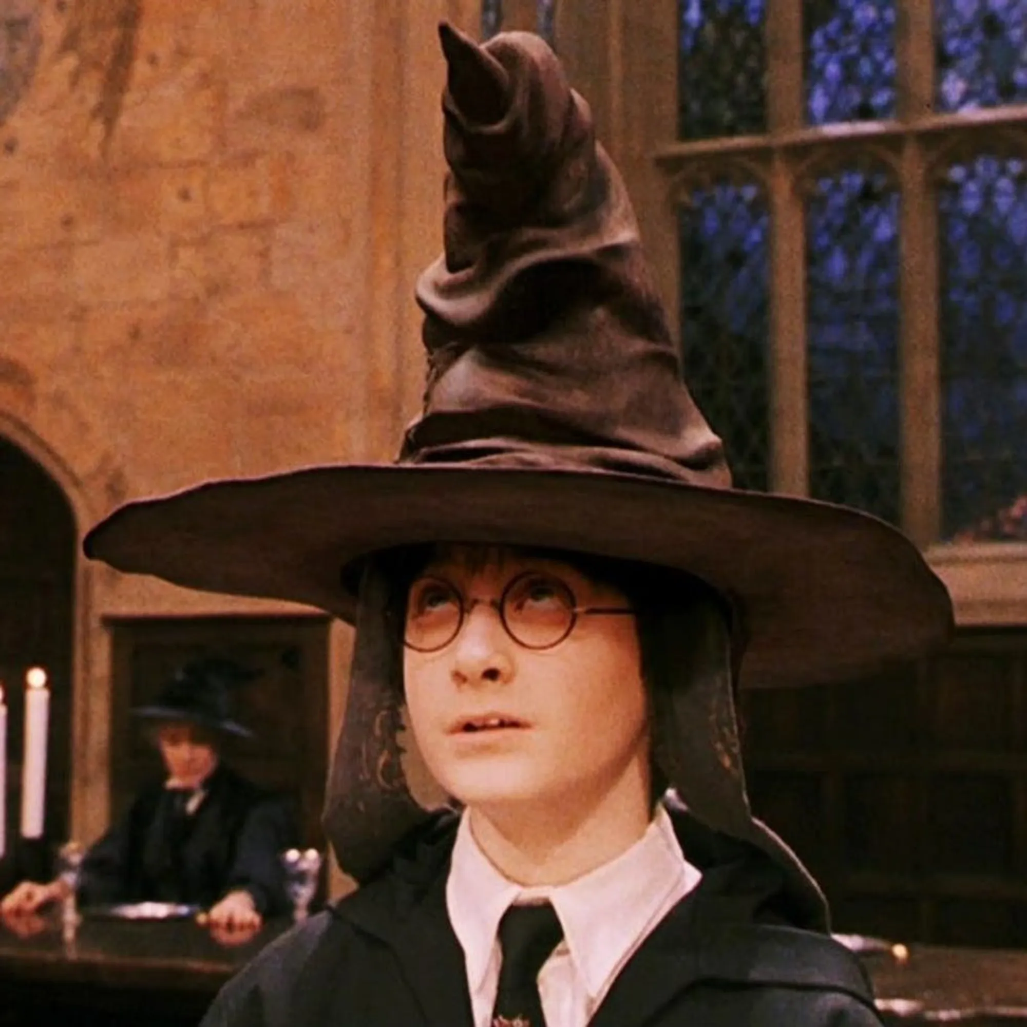 Sorting hat still from Harry Potter. A boy with round glasses wears a vaguely anthroporphised pointy hat that is way too large for him. He is looking up at the wide brim of the hat.