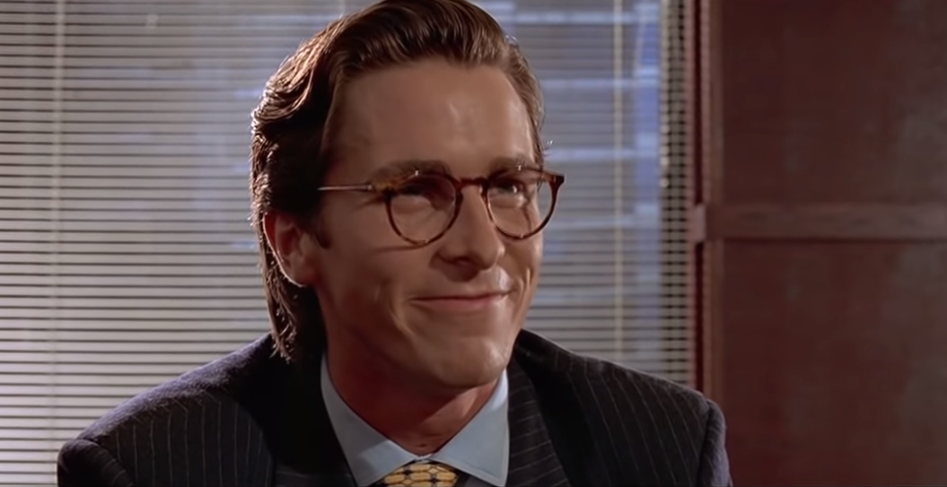 A photo of a stereotypical 1980s american yuppy in a suite and tie with glasses and a sarcastic grin ('Impressive. Very nice' meme from American Psycho)