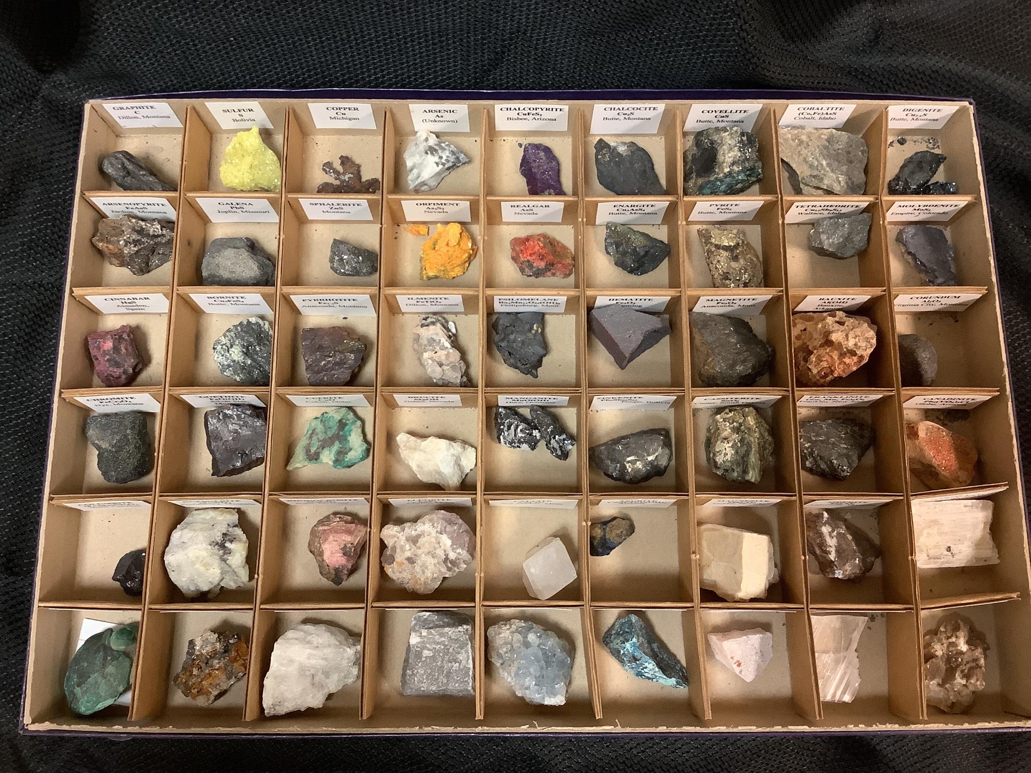 Photo of a box divided into dozens of small boxes, each containing a mineral sample (rock) and a label.