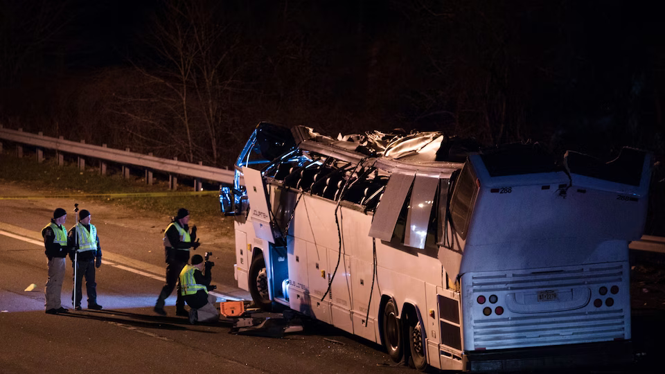 photograph of a emergency workers examining a damaged bus at night. The top of the bus appears to have been scraped partially off.