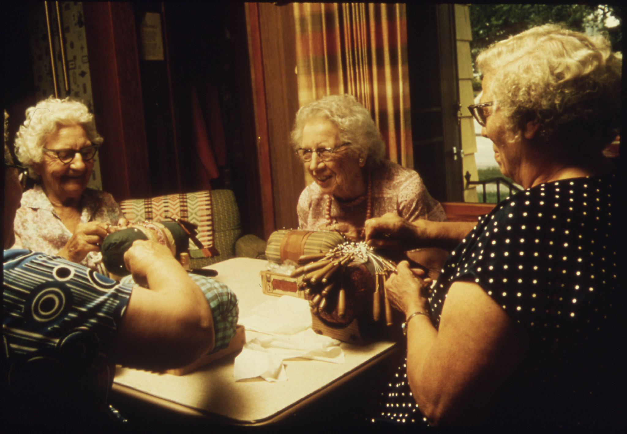 Photo of three older women collaboratively making lace around a table.