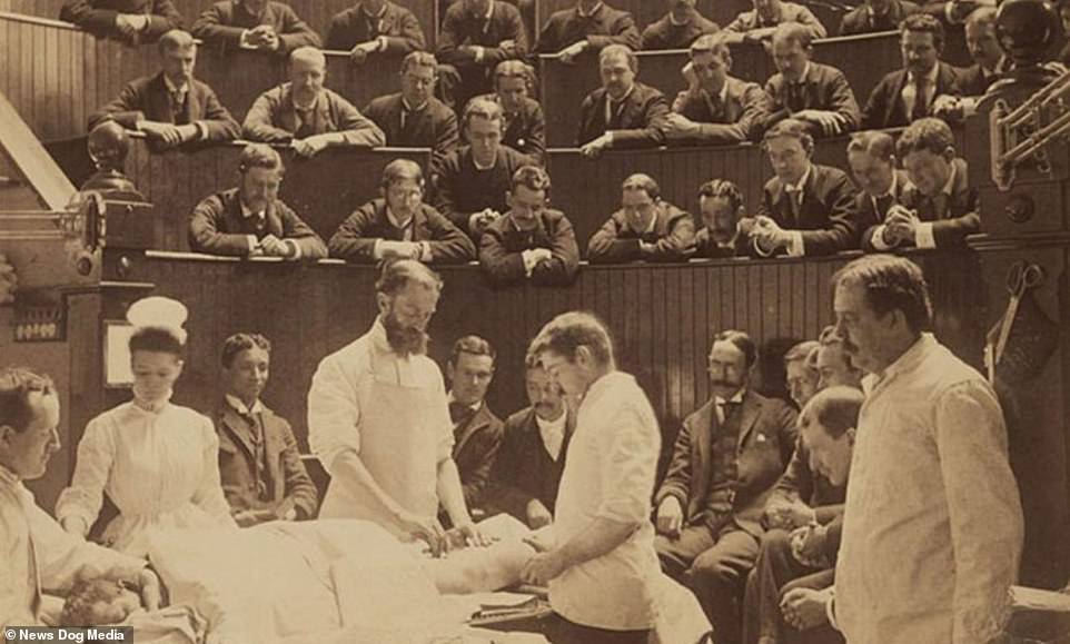 A sepia photo of an old-style operating theater, in which a large group of formallly dressed men watch a medical team perform surgery