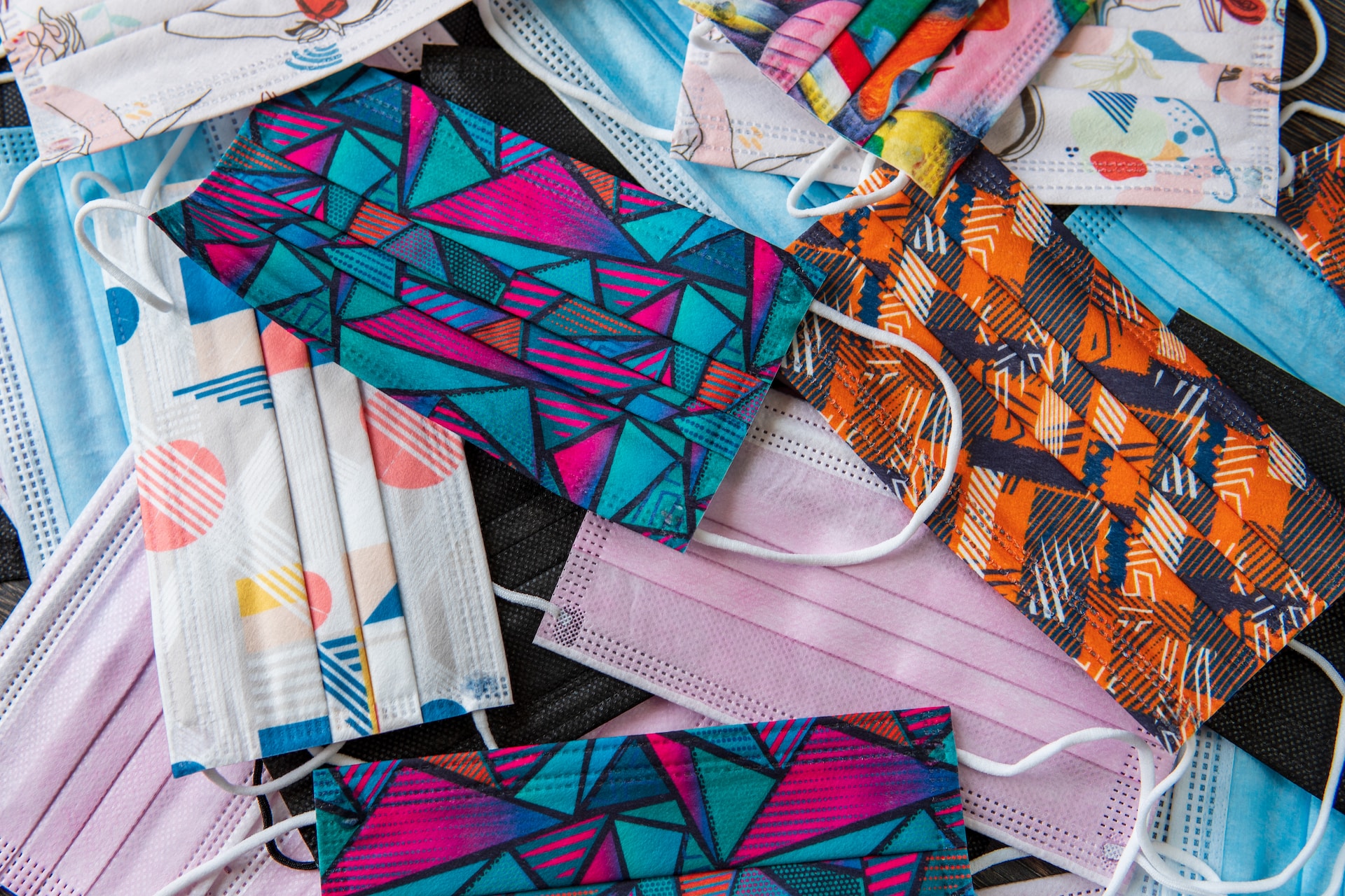A photograph of a pile of surgical masks with different colorful patterns on them.