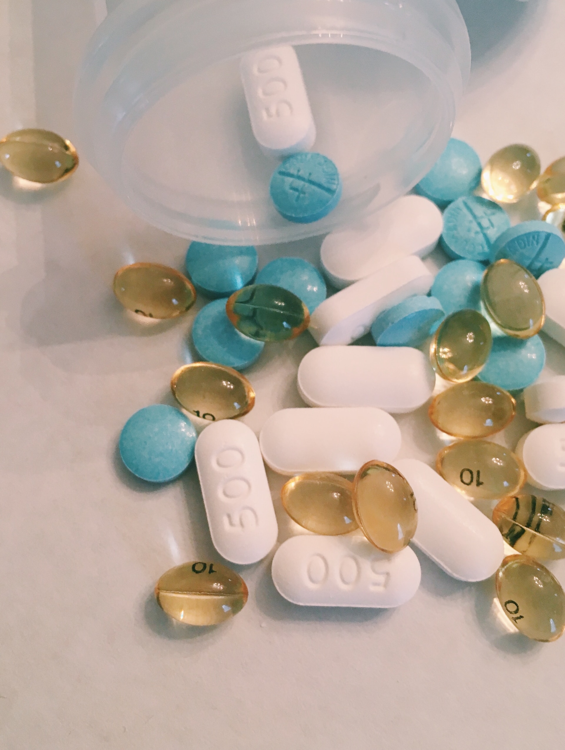 Photograph of three types of pills (blue round, white capsules, and transparent beads) spilling from an open pill bottle