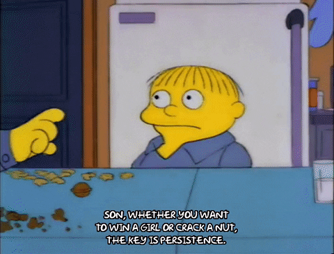Animation of Chief Wiggum from The Simpsons sitting at the a dining room table with his son. He is taking walnuts from a bowl and using the butt of his pistol to crack them open. Caption: 'Son, whether you want to win a girl or crack a nut, the key is persistence.'
